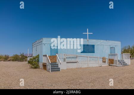 Una chiesa di rimorchio blu a Slab City, California, con una croce di legno bianca sulla parte superiore e con scale su entrambe le estremità. La chiesa è accessibile da ADA attraverso un lungo Foto Stock