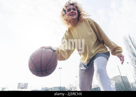 La giovane donna europea eccitata gioca a basket sul campo sportivo, cercando spazio copia medio full shot . Foto di alta qualità Foto Stock