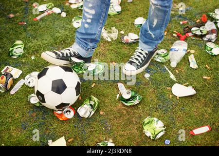 Calci intorno nel postumi. Una persona che gioca con un calcio in mezzo alla spazzatura lasciata dietro ad un festival musicale. Foto Stock