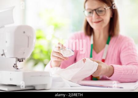 Donna che cucita alla scrivania bianca. Laboratorio di design della moda. Hobby creativo e artigianato. Concentratevi sulle mani. Luogo di lavoro su misura o a marinaio con overlock Foto Stock