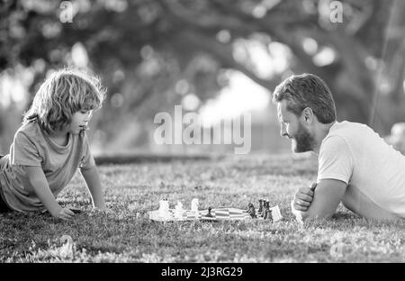 felice famiglia di papà e figlio bambino giocare a scacchi su erba verde nel parco all'aperto, gioco da tavolo Foto Stock