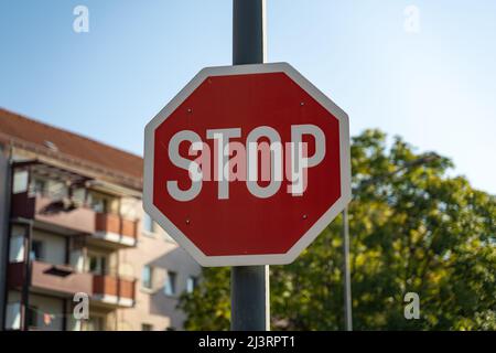 Un segnale di stop di fronte ad un albero e ad un edificio residenziale in una giornata di sole. Simboli del traffico in una città tedesca per rendere i conducenti di auto prudenti e attenti. Foto Stock