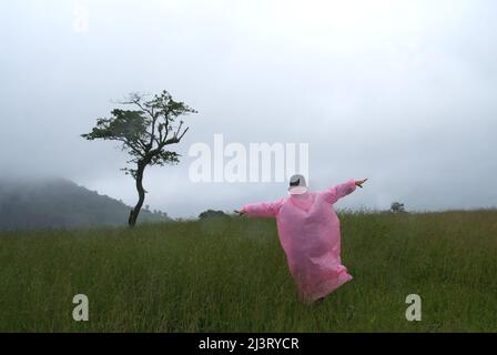 I turisti che indossano un impermeabile rosa si levano in piedi con le loro braccia fuori nell'erba in una giornata piovosa. Foto Stock