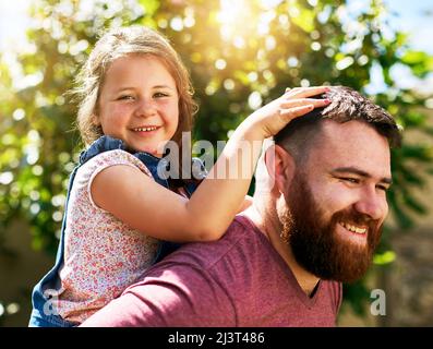 Rendendo la sua girlhood felice. Girato di una bambina adorabile godendo un giro di piggyback da suo padre nel loro cortile. Foto Stock