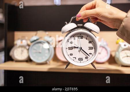 Sveglia rotonda in una mano della donna in primo piano. Vendita o acquisto di vari orologi e sveglie di diversi colori. Sveglia posteriore sul tavolo Foto Stock