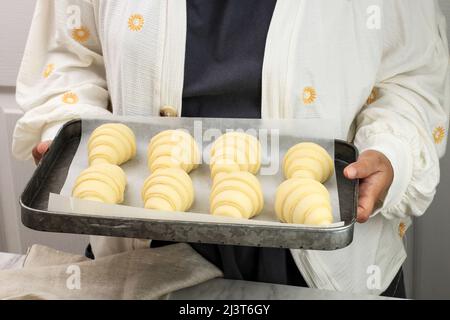 Pasta per croissant. Preparazione dei croissant. Teglia da forno femminile asiatica con croissant crudo, concetto di preparazione della panetteria Foto Stock