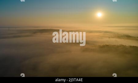 Al mattino all'alba sopra la nebbia. Paesaggio sopra un villaggio tra le foreste. Vista aerea. Foto Stock