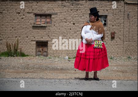 Jankho Amaya, Bolivia. 09th Apr 2022. Una donna, riconoscibile dal suo abbigliamento come autorità locale, guarda una corsa in bicicletta. La corsa 'Poncho rojo' (poncho rosso) attrae sia professionisti che dilettanti partecipanti e corre lungo le rive del Lago Titicaca ad altitudini che vanno da 3800 a 4000 metri. Quest'anno, oltre 450 ciclisti di tutte le età si sono registrati per l'evento, lungo 52 o 97 chilometri. Credit: Radoslaw Czajkowski/dpa/Alamy Live News Foto Stock