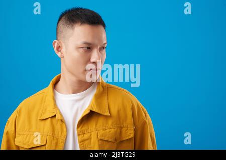 Ritratto di un giovane serio in giacca in denim senape e t-shirt bianca che guarda via Foto Stock