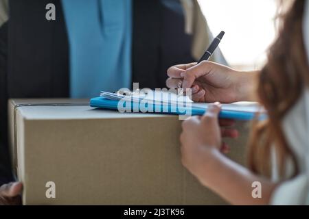 Ti preghiamo di firmare per accettare la consegna. Scatto corto di una donna che firma per un pacco consegnato da un corriere. Foto Stock