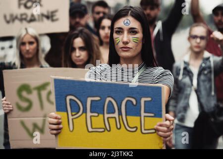 Pace giovani attivisti che protestano contro la guerra contro l'Ucraina. Concentratevi su una giovane donna che tiene un cartello con la bandiera e il mondo della Pace. Foto Stock