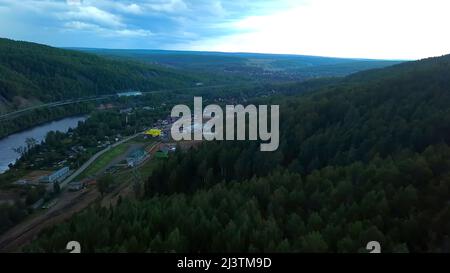 Vista dall'alto. Clip. Una bella foresta grande vicino a piccole case e una zona residenziale e un grande fiume lungo e un cielo luminoso dall'alto. Foto Stock