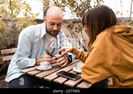 Coppia di giovani che guardano contenuti sullo smartphone seduti all'aperto Foto Stock