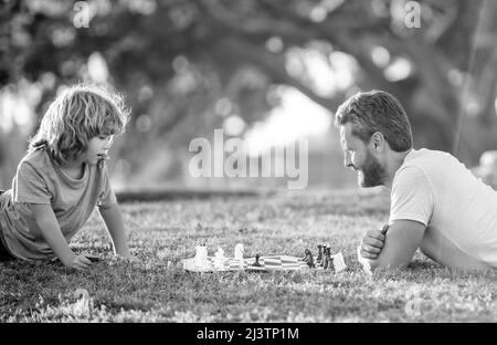 felice famiglia di papà e figlio bambino giocare a scacchi su erba verde nel parco all'aperto, gioco da tavolo Foto Stock