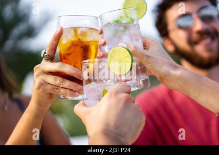 Gruppo di giovani amici che tostano all'aperto. Concentrati su occhiali, volti sfocati. Foto Stock