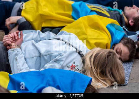 I manifestanti che hanno fatto un moriboire, facendo riferimento ai civili ucraini uccisi in città come Bucha durante la guerra con la Russia. Le femmine giocano morte con la bandiera Foto Stock