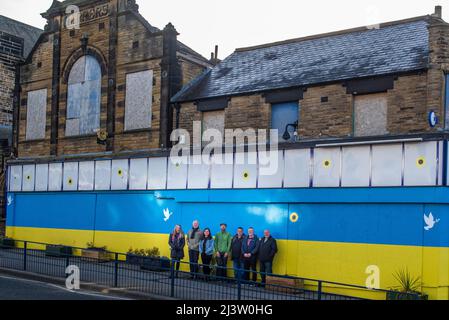 Starbeck, Harrogate, Regno Unito. 10th Apr 2022. Membri del gruppo della comunità di Starbeck Jill De Witt, Andrew Hart, Lucky Hubbard, Nik Mills, John Keane, David Stead e Colin Wilson hanno fotografato di fronte ad una bandiera Ucraina di 40 metri che hanno dipinto sopra l'edificio un tempo bello e ora derelitto di Harper su Starbeck High Street. Questo è uno dei molti progetti su cui stanno lavorando per rivitalizzare e motivare la loro comunità locale. Credit: ernesto rogata/Alamy Live News Foto Stock