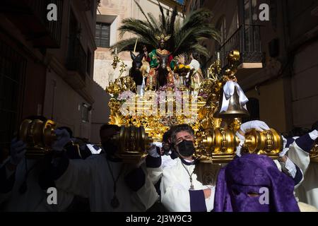 I Penitenti della fraternità “Pollinica” sono visti portare un galleggiante ornato con la statua di Cristo e della Vergine Maria mentre prendono parte ad una processione la Domenica delle Palme, in occasione delle celebrazioni della settimana Santa. Dopo due anni senza la settimana Santa a causa della pandemia del coronavirus, migliaia di fedeli attendono di vedere le processioni che portano le statue di Cristo e della Vergine Maria per le strade come parte della settimana Santa tradizionale. In Andalusia, la celebrazione della settimana Santa accoglie migliaia di persone provenienti da tutti i paesi, ed è considerata uno dei più importanti eventi religiosi e culturali dell'anno. Foto Stock