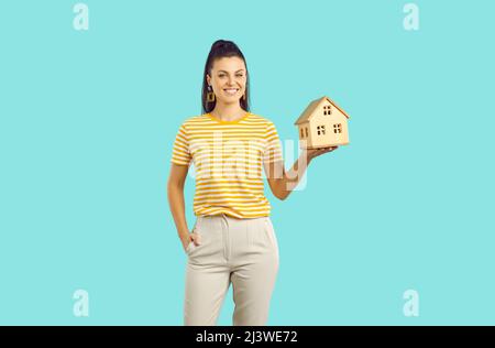 Donna su sfondo colorato tiene piccola casa come simbolo di costruzione o prestito per comprare casa. Foto Stock