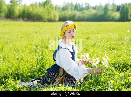 Giovane donna in abito nazionale in un campo con fiori di naffodils Foto Stock