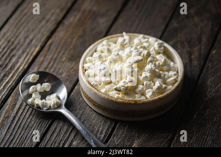 Contadini ricotta formaggio in una ciotola di argilla, accanto ad un cucchiaio su sfondo di legno scuro, Close-up. Naturale cibo sano, sano cibo sano sano sano Foto Stock