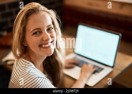 Mettendo in uno sforzo A+. Ritratto di una giovane studentessa felice che usa il suo laptop per studiare al tavolo di un caffè. Foto Stock