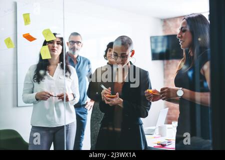 Gruppo di uomini d'affari che condividono le loro idee in un ufficio. gli uomini d'affari attaccano le note adesive a una parete di vetro mentre fanno brainstorming con un wor creativo Foto Stock
