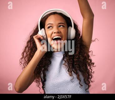 Quando ti senti giù, un buon battito ti solleverà. Studio girato di una bella giovane donna che indossa le cuffie mentre si alza contro un rosa Foto Stock