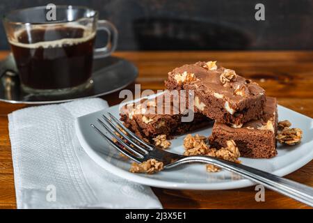 Quadrati di brownie al cioccolato fatti in casa con pezzi di pecan serviti su un piatto bianco. Concetto di cibo naturale e sano. Vista alta. Foto Stock