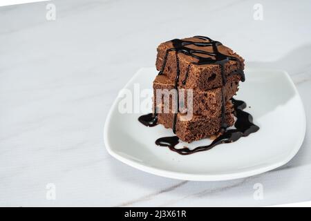 mucchio di brownie di cioccolato con ciocche di salsa di cioccolato su un piatto bianco su un tavolo di marmo. Spazio di copia. Foto Stock