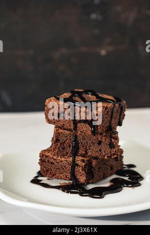 pelo di brownie di cioccolato con ciocche di salsa di cioccolato su un piatto bianco su un tavolo di marmo. orientamento verticale. Spazio di copia. Foto Stock
