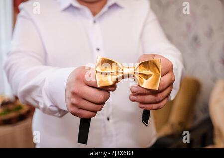 Cravatta d'arco d'oro nelle mani dello sposo. Arco cravatta nelle mani di un uomo Foto Stock