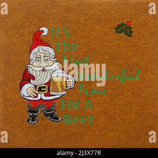 Babbo Natale che tiene la tazza di birra, testo è il momento più meraviglioso per una birra, parole, ricamo a macchina, tessuto, colorato, appendiabiti, fibre art, c Foto Stock