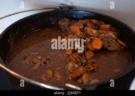 Guance di manzo brasate che cucinano in salsa di vino rosso nel forno olandese in ghisa. Stufato di carne cotto lento. Foto Stock