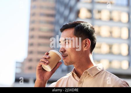 Un giovane uomo d'affari sorsegge il caffè in città, lavorando sodo Foto Stock