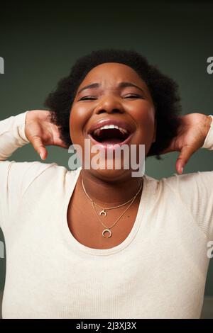 Vivere, ridere, amore. Scatto di una giovane donna attraente ridendo mentre si posa su uno sfondo verde in studio. Foto Stock