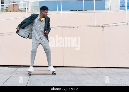 giovane uomo d'affari che guida uno skateboard in un vestito Foto Stock