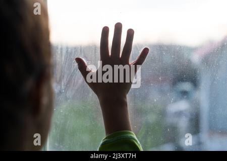 Ragazza giovane a mani finestra premuto contro finestra, pensivo o volendo fuori Foto Stock