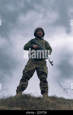 Il soldato ucraino è in piedi con il fucile d'assalto kalashnikov nelle sue mani sullo sfondo del cielo e delle nuvole. Concetto di invasione militare russa in Ukr Foto Stock