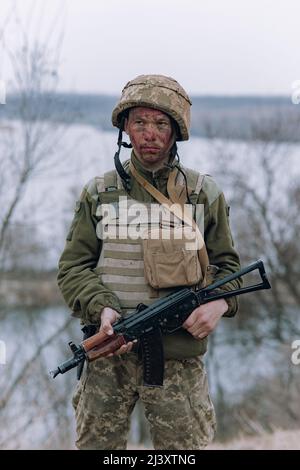 Il soldato ucraino è in piedi con il fucile d'assalto kalashnikov nelle sue mani sullo sfondo del cielo e del fiume. Concetto di invasione militare russa in Ukra Foto Stock