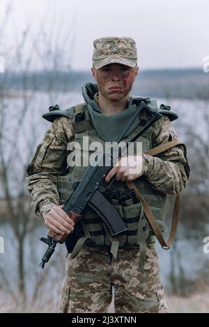 Il soldato ucraino è in piedi con il fucile d'assalto kalashnikov nelle sue mani sullo sfondo del cielo e del fiume. Concetto di invasione militare russa in Ukra Foto Stock