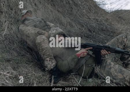 Due soldati ucraini si trovano con fucili d'assalto kalashnikov sull'erba secca durante il bombardamento di artiglieria da parte del nemico russo. Concetto di inv. Militare russo Foto Stock