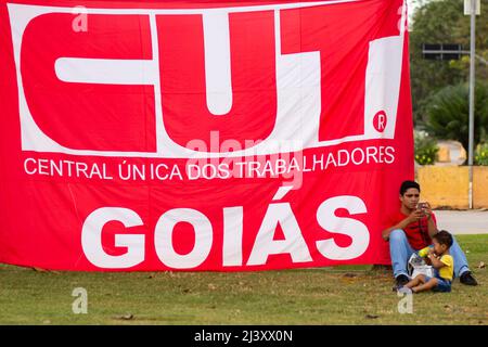 Goiânia, Goias, Brasile – 09 aprile 2022: Un uomo con un bambino seduto sotto una bandiera TAGLIATA. Foto scattata durante una protesta, nella città di Goiânia. Foto Stock