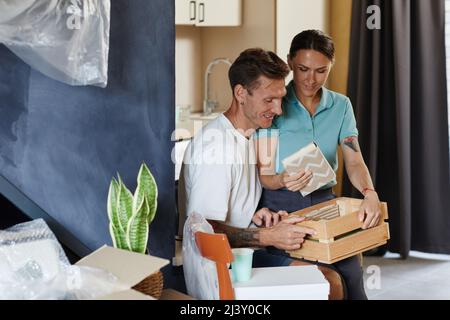 Vista laterale ritratto di tatuato giovane coppia disimballaggio scatole in nuova casa e sorridente, spazio copia Foto Stock