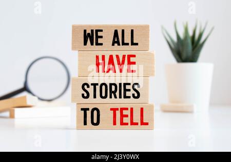 Tutti abbiamo storie da raccontare Symbol. Blocchi di legno con parole 'abbiamo tutti storie da raccontare'. Mano uomo d'affari. Splendido sfondo grigio. Business, pop Foto Stock