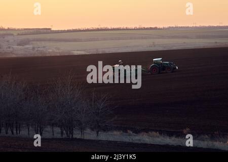Il trattore aratri il campo agricolo al tramonto in autunno Foto Stock