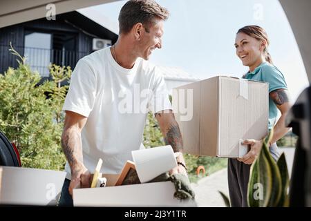 Basso angolo ritratto di felice giovane coppia caricando scatole in bagagliaio auto mentre si sposta in nuova scena casa alla luce del sole Foto Stock