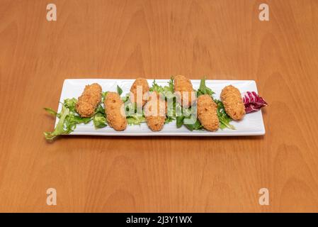 Deliziose e tipiche crocchette spagnole di prosciutto serrano su un letto di lattuga servite in un ristorante di tapas spagnole Foto Stock