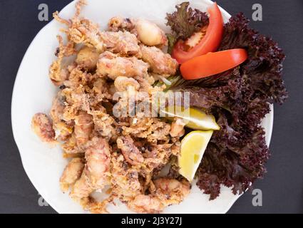 Vista dall'alto di calamari fritti sul piatto con limone, lattuga e pomodoro. Tradizionale tapa di pesce spagnolo Foto Stock