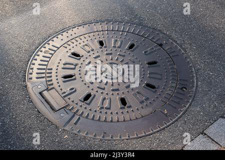 vista laterale del coperchio in ferro di una botola impermeabile in una strada della città alla luce del sole serale Foto Stock